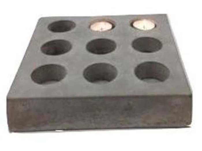 En rektangulær grå blok med ni runde huller, hvoraf to indeholder små tændte fyrfadslys.