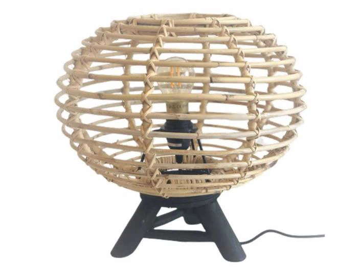 Rund bordlampe i rattan med en vævet, åben kugleskærm, sort trefodsfod og synlig pære indeni.