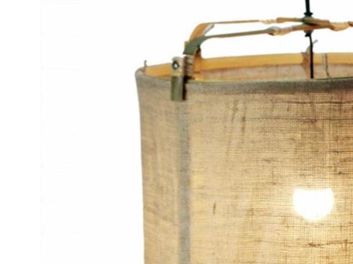 Nærbillede af en hængelampe med en rund, beige stofskærm og synlig metalramme, oplyst af en pære indeni.