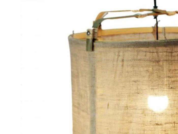 Nærbillede af en hængelampe med en rund, beige stofskærm og synlig metalramme, oplyst af en pære indeni.