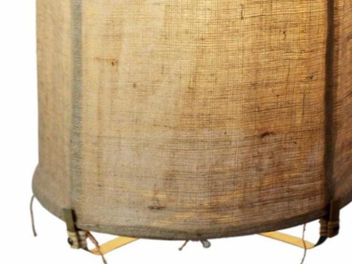 Et nærbillede af den nederste del af en cylindrisk lampe med en struktureret beige stofskærm og tynde metalben.