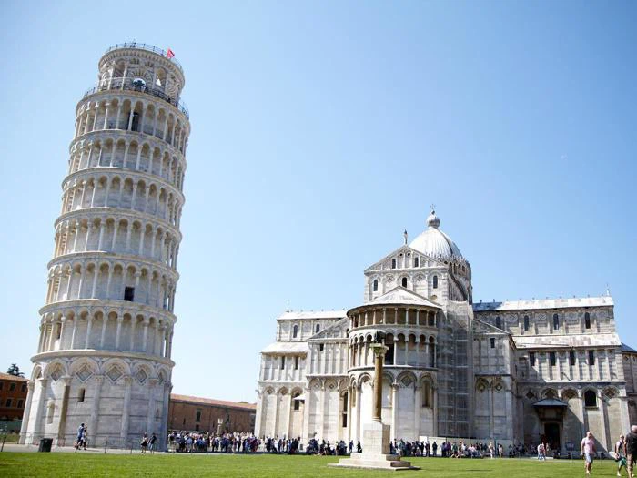 Det skæve tårn i Pisa og katedralen i Pisa i Italien, med en klar blå himmel og grupper af turister samlet omkring vartegnene.