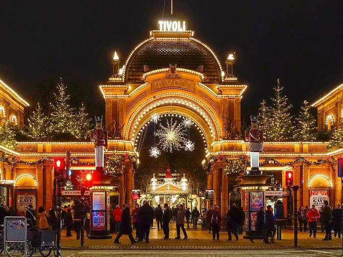 Feststemte mennesker samles ved den oplyste indgang til Tivoli i København, der er udsmykket med julelys, træer og dekorationer om aftenen.