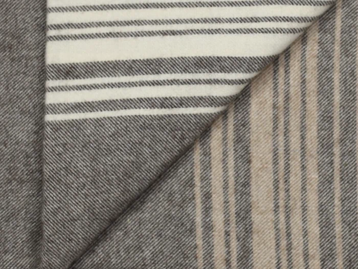 Et nærbillede af to stykker stof med diagonal fold; det ene har sorte og hvide striber, det andet har sorte og beige striber, begge på en grå baggrund.