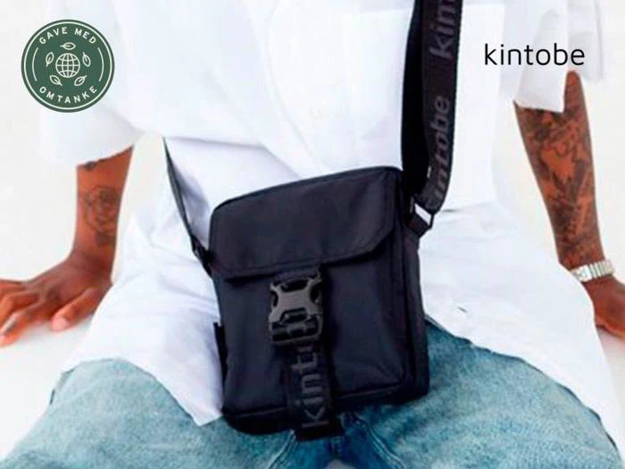 En person iført hvid skjorte, blå jeans og en sort crossbody-taske sidder med hænderne på knæene. Der står kintobe på tasken. Der er et grønt rundt logo og kintobe-tekst på billedet.