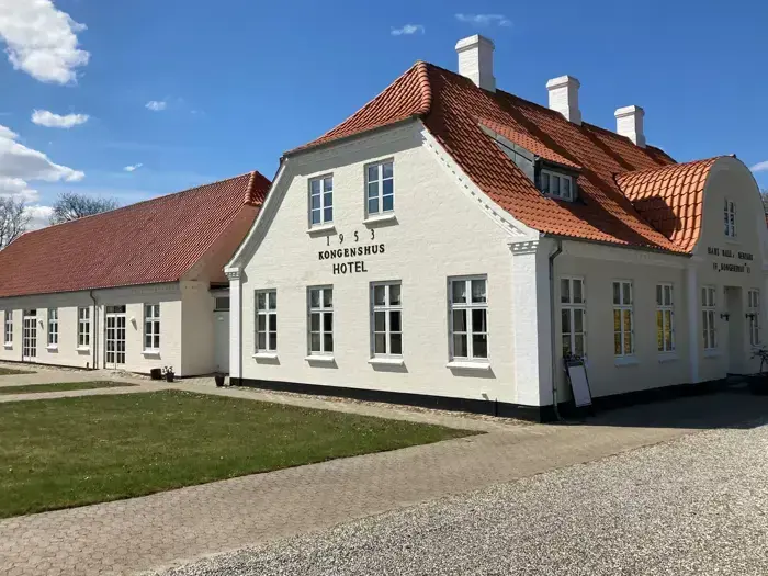 En hvid bygning med rødt tegltag og et skilt med teksten Kongenshus Hotel under en blå himmel med spredte skyer.
