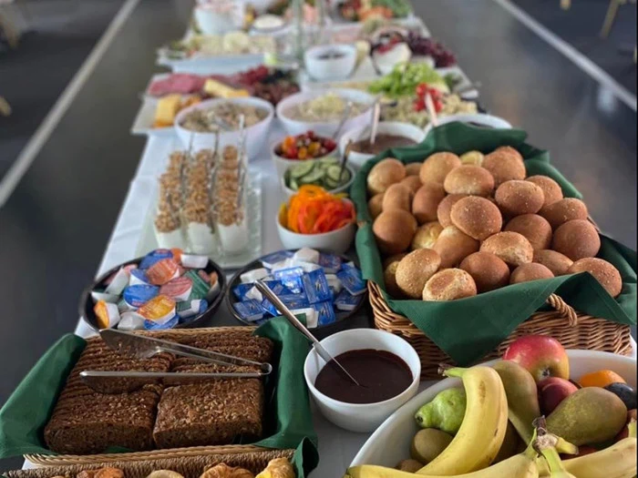 Et bord fyldt med forskelligt brød, frugt, granola, smørepålæg, salater, grøntsager og forskellige morgenmadsprodukter, opstillet som en buffet til et måltid.