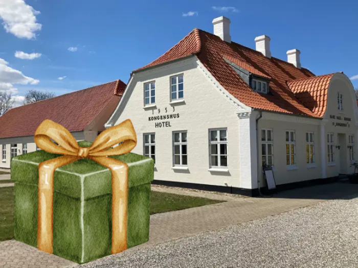 En stor grøn gaveæske med et guldbånd er tilføjet digitalt foran en hvid bygning med rødt tag under en blå himmel.