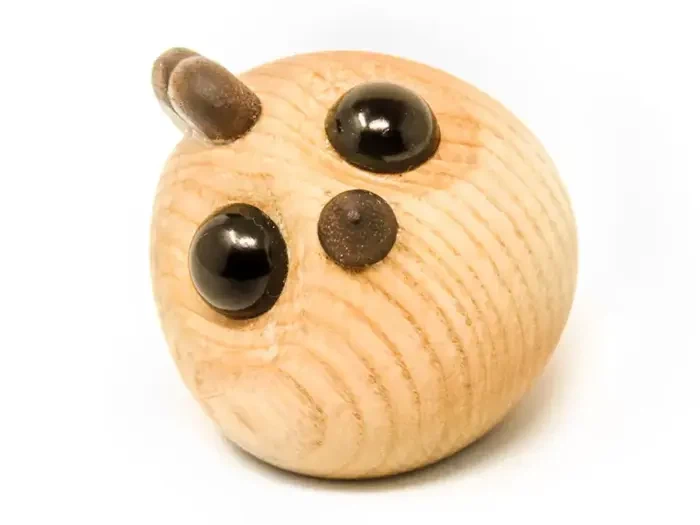 En lille, rund trægenstand med to store sorte øjne og to små ører, der ligner et abstrakt dyr, på en hvid baggrund.