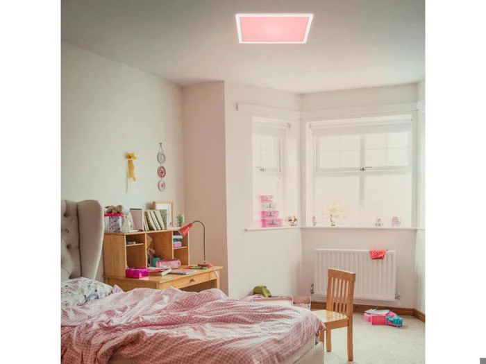 Et hyggeligt soveværelse med en rodet seng, træskrivebord og stol. Lyserød indretning præger rummet, og en blød lyserød loftslampe oplyser rummet. Sollyset trænger ind gennem to store vinduer.