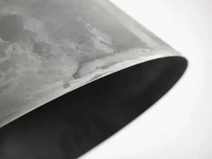 Nærbillede af kanten af et buet, metallisk, sølvgråt rør med en let forvitret overflade.