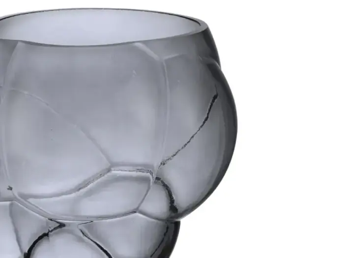 Nærbillede af et gråt glas med en struktureret, facetteret overflade, der ligner et fodboldmønster, på en hvid baggrund.
