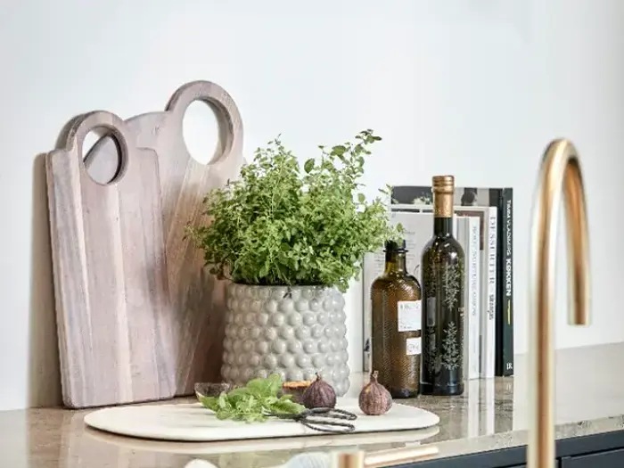 Skærebrætter, en potteplante, to flasker olie, kogebøger og figner er arrangeret pænt på køkkenbordet.