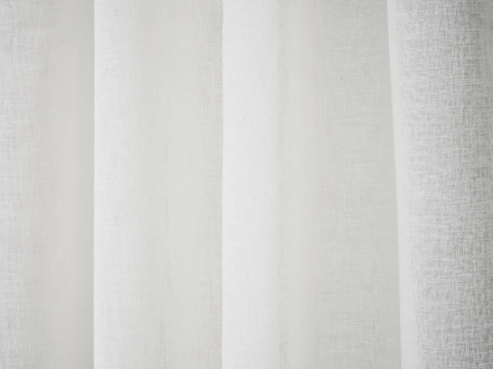 Nærbillede af hvide gardiner, der hænger i bløde folder, så lyset forsigtigt filtreres gennem stoffet.