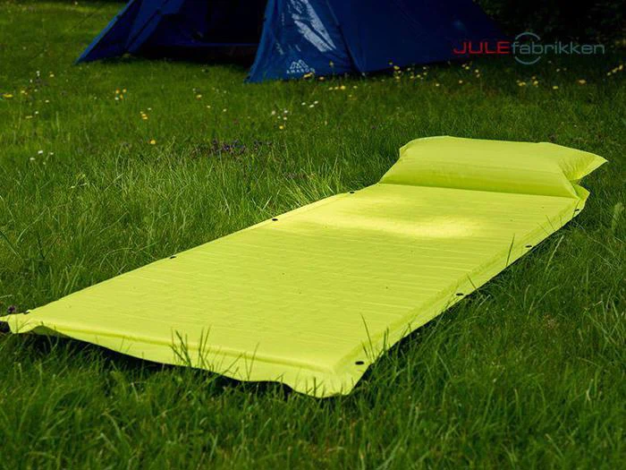 En knaldgul campingmåtte med en tilhørende pude ligger på grønt græs med et blåt telt i baggrunden.