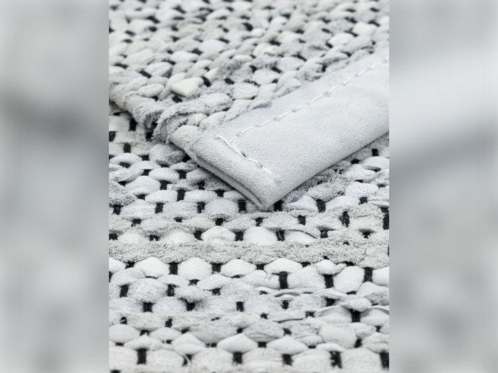 Nærbillede af et vævet stof med en foldet kant, der viser et struktureret mønster af sammenflettede lyse og mørke tråde og synlige syninger.