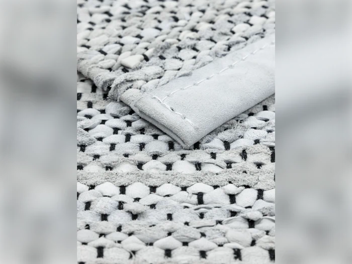 Nærbillede af et vævet stof med en foldet kant, der viser et struktureret mønster af sammenflettede lyse og mørke tråde og synlige syninger.