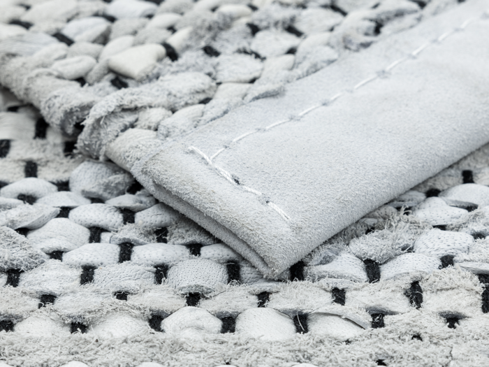 Nærbillede af et struktureret, vævet stof i grå og hvide nuancer, der viser et foldet hjørne med synlige syninger.