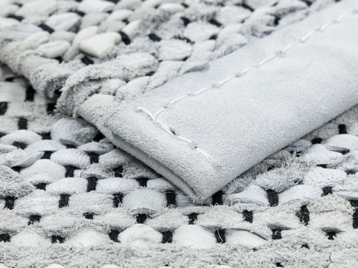 Nærbillede af et struktureret, vævet stof i grå og hvide nuancer, der viser et foldet hjørne med synlige syninger.