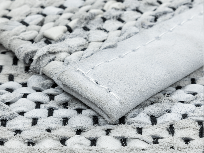 Nærbillede af et vævet gråt tekstil med en syet stofstrimmel ovenpå, der viser detaljeret tekstur og syninger.