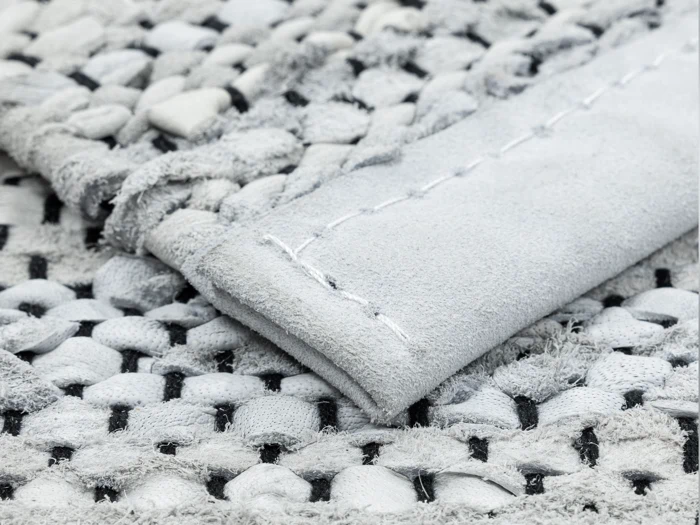 Nærbillede af et vævet gråt tekstil med en syet stofstrimmel ovenpå, der viser detaljeret tekstur og syninger.