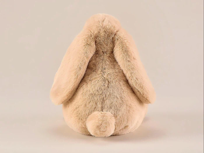 En plysdyrkanin set bagfra, med hængeører og en lille rund hale, lavet af blød beige pels, på en ensfarvet baggrund.