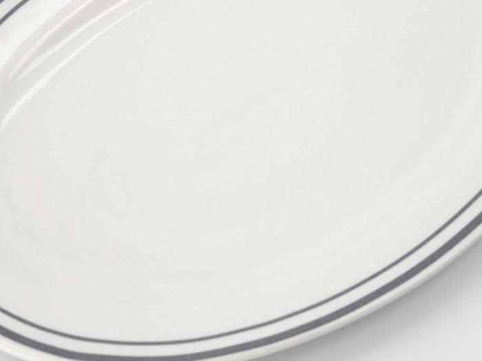 Et nærbillede af en hvid keramiktallerken med to tynde, mørkeblå linjer nær kanten.