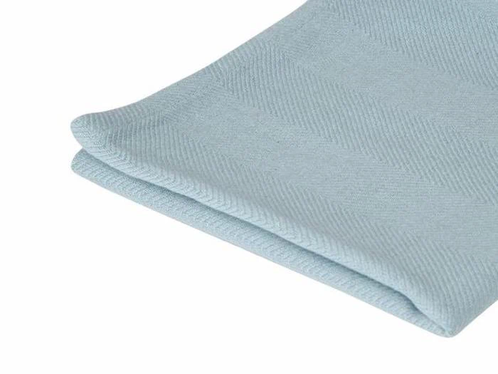 Et nærbillede af en pænt foldet lyseblå stofserviet med et diskret sildebensmønster, placeret på en hvid baggrund.