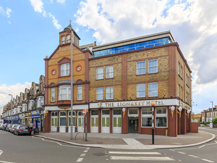 En treetagers murstensbygning med The Lion & Key Hotel-skiltet i stueetagen, der ligger på et gadehjørne under en delvis overskyet himmel.