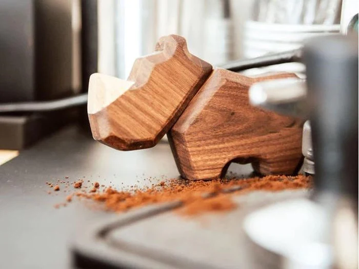 En flodhestefigur af træ på en bordplade med spredt kaffegrums i nærheden.