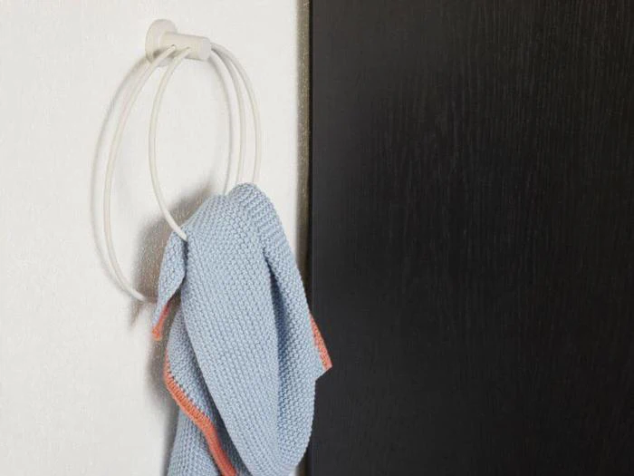 Et blåt håndklæde med en orange kant hænger på en hvid, rund håndklædering, der er monteret på en hvid væg ved siden af en mørk dør eller et mørkt panel.