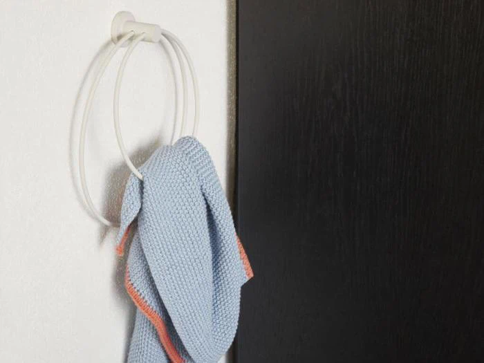 Et blåt håndklæde med en orange kant hænger på en hvid, cirkulær håndklædeholder, der er monteret på en hvid væg ved siden af en mørk dør.