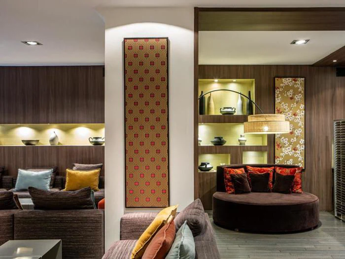 En moderne lounge med brune sofaer, farverige puder, dekorative hylder med keramik, mønstrede vægpaneler og varm belysning.