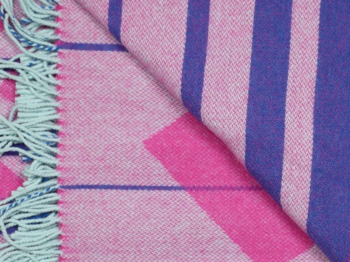 Nærbillede af et vævet stof med pink og lilla geometriske mønstre og lyseblå frynser på den ene kant.