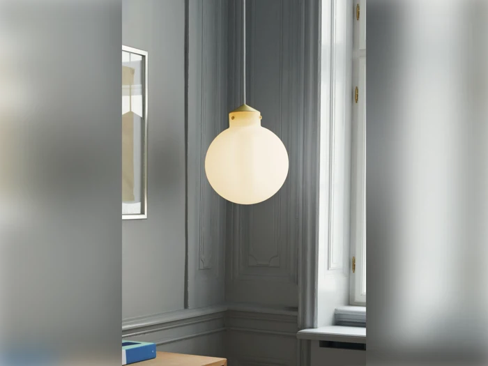 En rund, hvid pendel hænger fra loftet i et rum med grå vægge og dekorative lister ved siden af et vindue og et indrammet kunstværk.