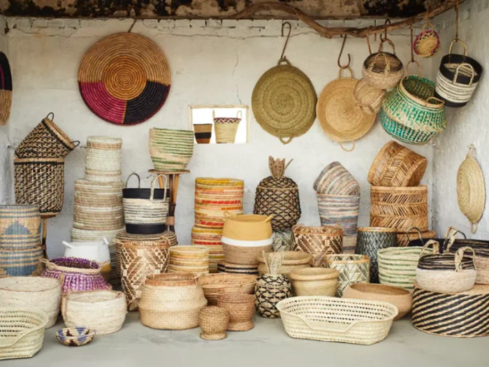 En række farverige, håndvævede kurve er stablet og hængt op på væggene i et rustikt rum, hvor de fremviser forskellige former, størrelser og mønstre.