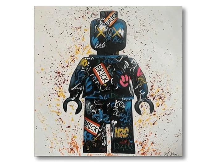 En farverig figur i LEGO-stil er dækket af graffiti og tags og står på en hvid baggrund, der er oversprøjtet med forskellige farver maling.