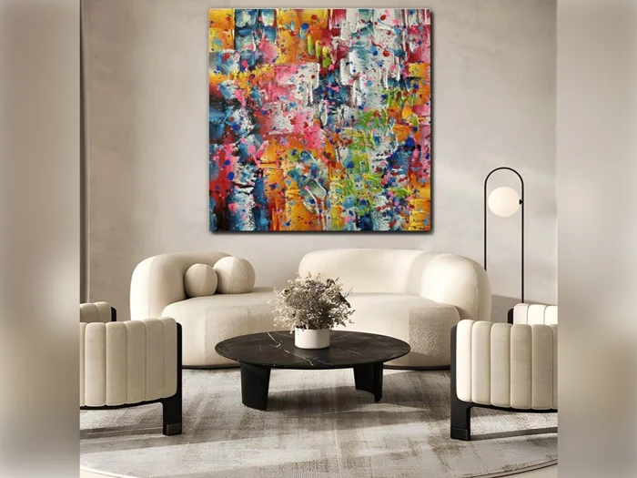 Moderne stue med cremefarvede sofaer og stole, et sort, rundt sofabord og et farverigt, abstrakt maleri på den beige væg.