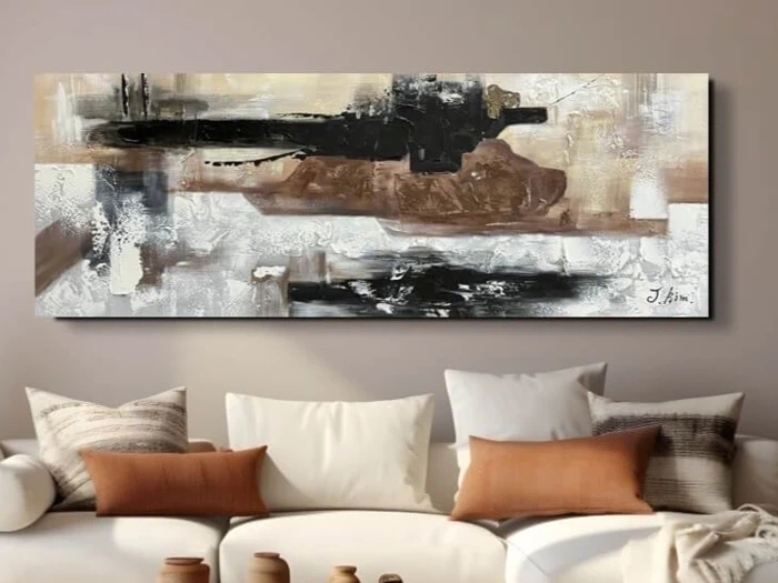 Et abstrakt maleri med sorte, brune og hvide penselstrøg hænger over en beige sofa med forskellige puder i neutrale farver.