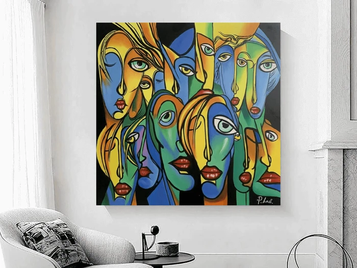 Farverigt abstrakt maleri af overlappende, langstrakte ansigter med kraftige røde læber og udtryksfulde øjne, der hænger på en hvid væg over en moderne stol og et sidebord.