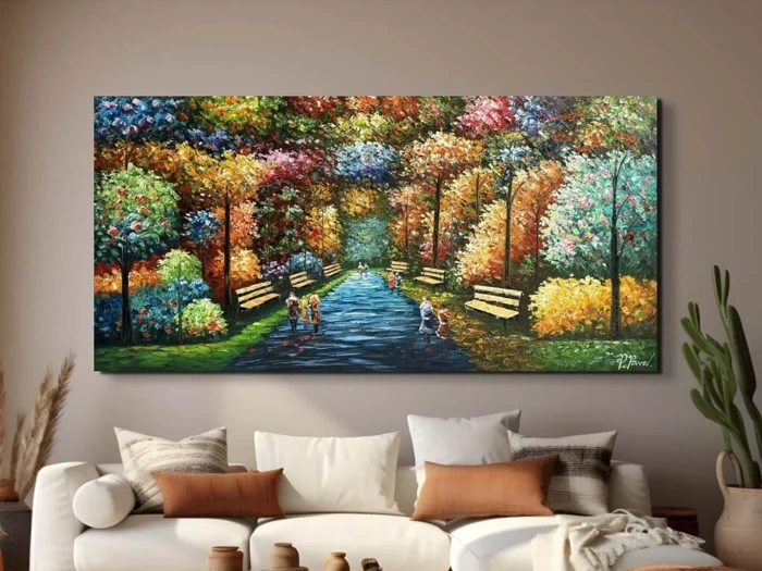 Et farverigt maleri af mennesker, der går i en park med træer og bænke, hænger over en beige sofa med hvide og brune puder i en hyggelig stue.
