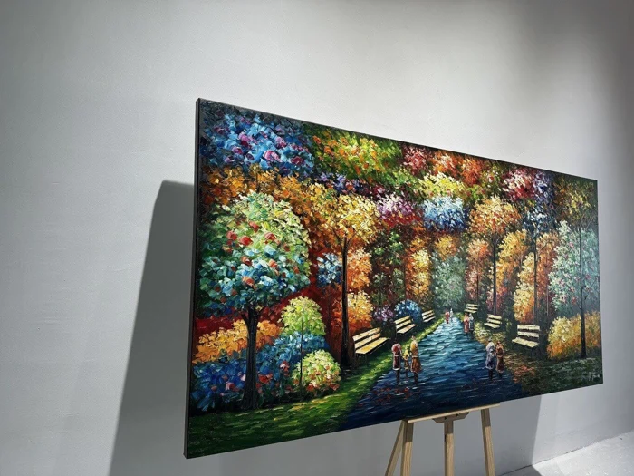 Et farverigt maleri på et staffeli forestiller en parkscene med træer, bænke og mennesker, der går langs en sti, oplyst af sollys.