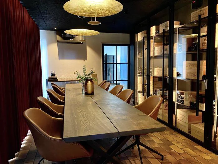 En moderne spisestue med et langt træbord, solbrune stole, varm belysning, et vinskab og en glasdør i baggrunden.