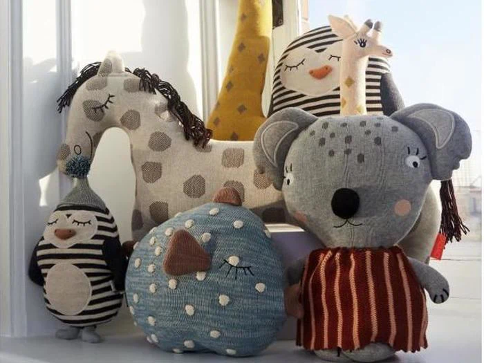 En gruppe udstoppede legetøjsdyr, herunder en giraf, en pingvin, en ugle, en blå fugl og en koala, er arrangeret sammen ved et solbeskinnet vindue.