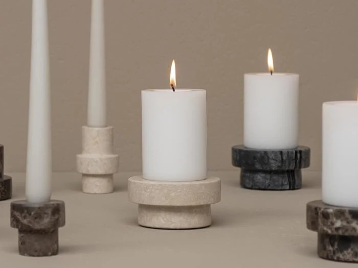 Flere hvide lys, nogle tændte og andre utændte, er placeret i runde stenlysestager i forskellige nuancer på en neutralfarvet overflade mod en beige baggrund.
