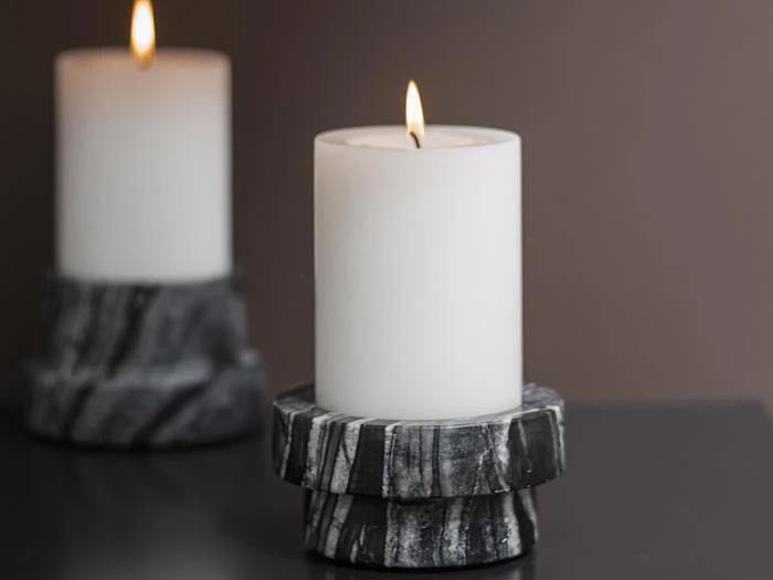 Et hvidt bloklys, der brænder på en sort og hvid marmoreret holder, med et andet utændt lys i den slørede baggrund.