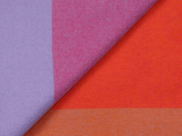 Et nærbillede af stof med krydsende blokke af lilla, pink, rød og orange farver, foldet diagonalt hen over billedet.