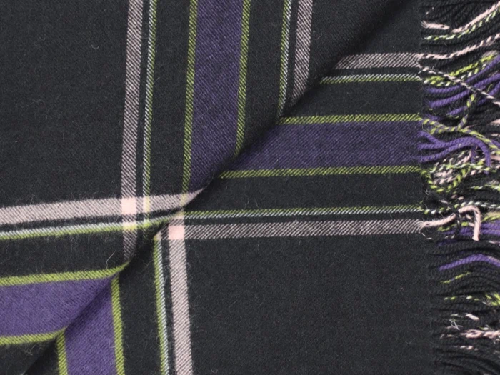 Et nærbillede af et ternet stof med sorte, lilla, grønne og hvide striber med frynsede kanter i højre side.