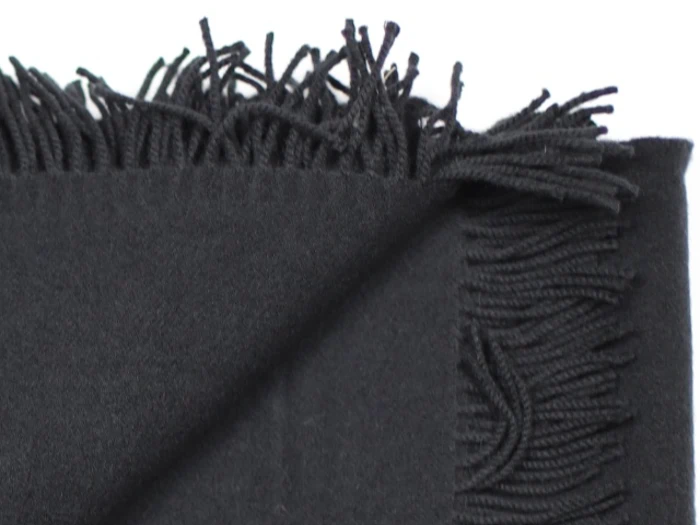Et nærbillede af et sort uldtørklæde med frynsede kanter, foldet i hjørnet for at vise strukturen og kvasterne.
