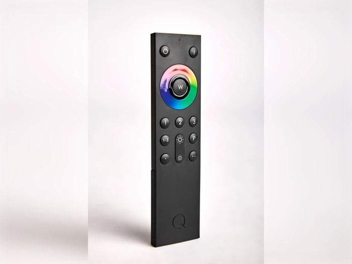 En sort fjernbetjening med en cirkulær, flerfarvet knap øverst og flere sorte knapper nedenunder, der står oprejst mod en hvid baggrund.